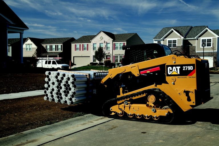 Picture of a CAT Skid Steer using the fork lift to move a full load of residential pipe.